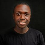Close-up portrait of a smiling young African man in a black shirt against a dark background.